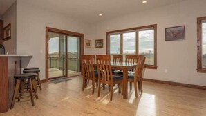 Un comedor con mesa y sillas de madera, una barra de cocina con taburetes y amplios ventanales con vistas.