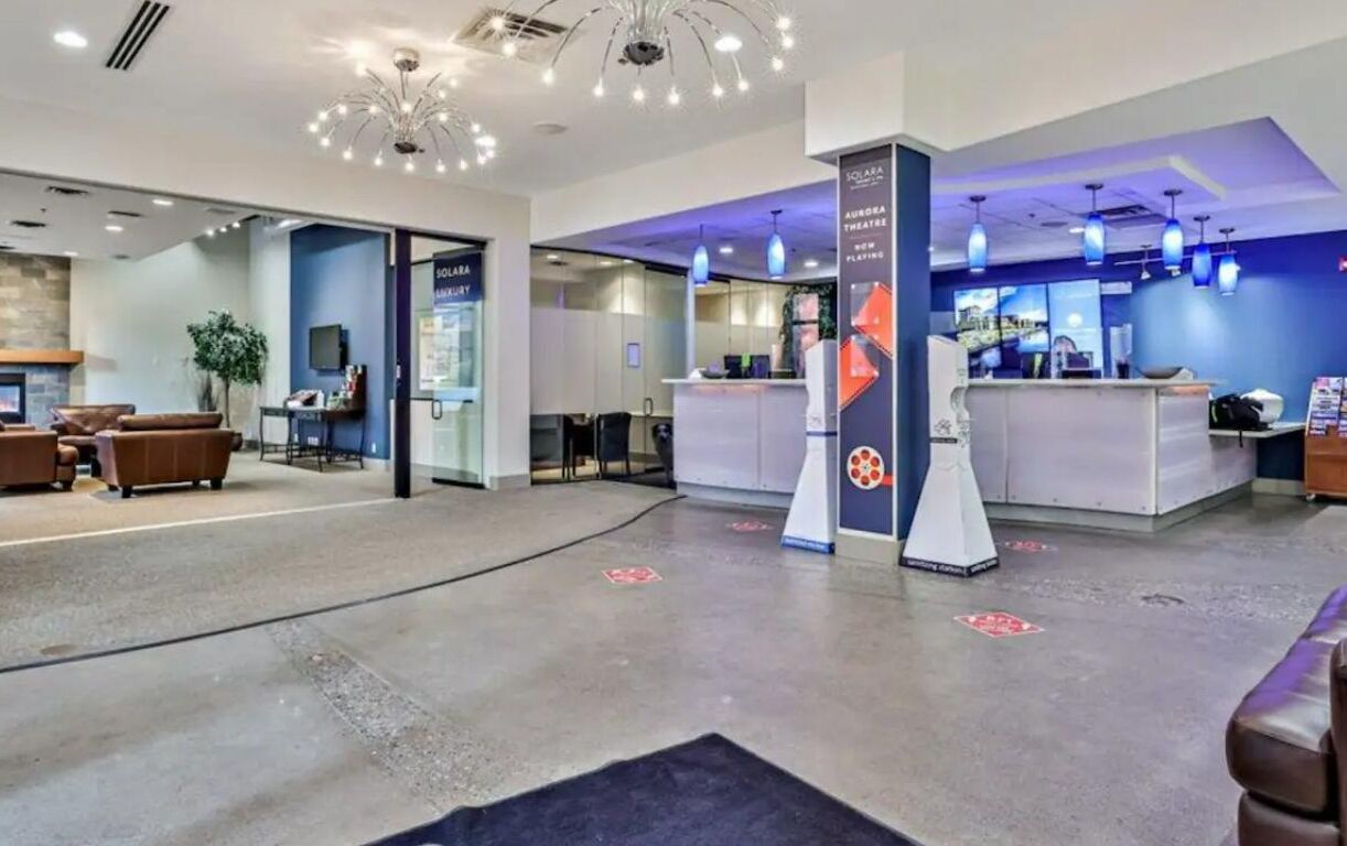 Eine moderne Hotellobby mit Empfangstresen, Sitzgelegenheiten und einem großen Kronleuchter.