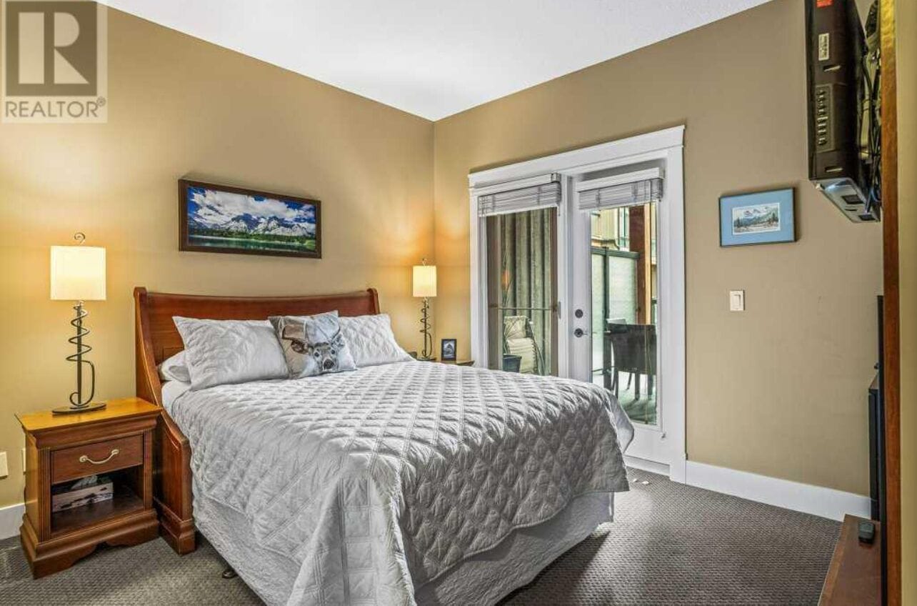 A bedroom with a large bed, two bedside tables with lamps, a window with a view, and a door leading to a balcony.