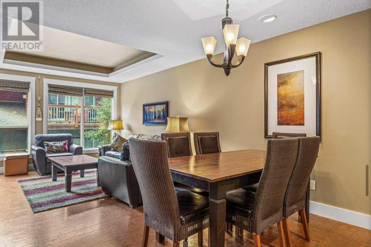 A dining area with a wooden table and chairs, a chandelier, and a large window with a view of a building.