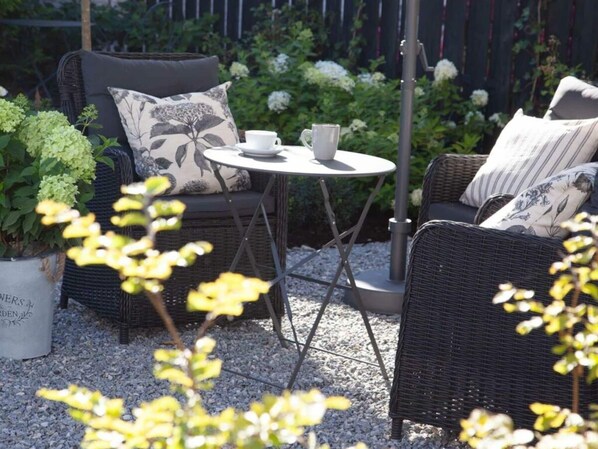Un coin salon extérieur aménagé avec des meubles en osier, comprenant une table ronde, deux chaises et un pot de fleurs.