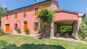 Una villa rosa con un porche cubierto, escalones de piedra y un pequeño jardín.