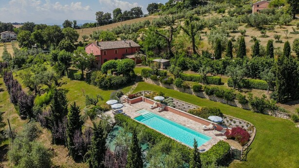 Una gran piscina rectangular rodeada de césped y jardín cuidados, con un edificio rojo al fondo.