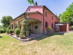 Une maison rose avec un porche abrité, des murs en pierre et des plantes en pot.
