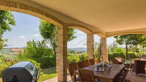 Un patio al aire libre con suelo de ladrillo, mesa y sillas de madera, con vistas a un paisaje pintoresco.
