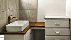 Un baño con un lavamanos blanco, un grifo dorado y una encimera de madera. Hay tres cajones debajo del lavamanos.