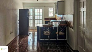 Una cocina con una isla central, dos taburetes de bar y un refrigerador.