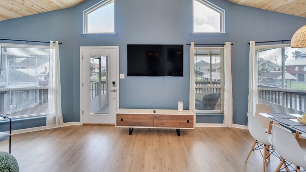 A modern living room with a large TV, wooden ceiling, and large windows. - Waterfront, King Suite, Fully Stocked, Minutes from New Orleans, Pets Welcome (Barataria)