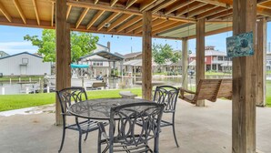 A covered patio with a table and chairs, a swing, and a view of a residential area with houses and a body of water. - Waterfront, King Suite, Fully Stocked, Minutes from New Orleans, Pets Welcome (Barataria)