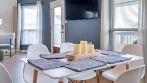 A modern living room with a flat-screen TV mounted on the wall, a dining table with candles, and a sofa. - Waterfront, King Suite, Fully Stocked, Minutes from New Orleans, Pets Welcome (Barataria)