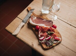 A wooden cutting board with a steak, prosciutto, radishes, and herbs on a table. - Appartementencomplex Titisee (Titisee-Neustadt)