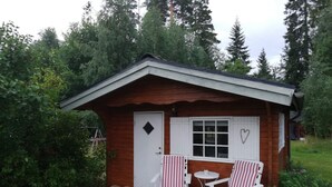 A small wooden cabin with a porch, two striped chairs, and a small table. - 4 Star Holiday Home in Skutskar-by Traum (Alvkarleby)