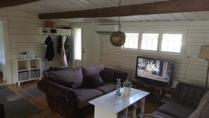 A cozy living room with a sofa, a coffee table, and a television. There is a window with curtains, a hanging light fixture, and a shelf with items. - 4 Star Holiday Home in Skutskar-by Traum (Alvkarleby)