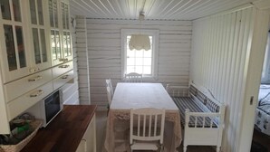A small, compact room with a wooden floor, a white table with a lace tablecloth, a white bench with a plaid cushion, and a white cabinet with glass doors. - 4 Star Holiday Home in Skutskar-by Traum (Alvkarleby)