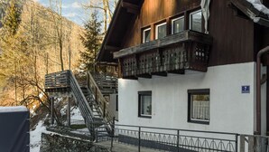 Eine Holzhütte mit Balkon, Steinstufen und Blick auf einen verschneiten Berg.