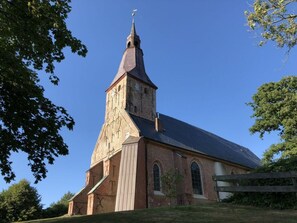 A church with a tall steeple and a brick facade. - Nordseeestate Comfortable Holiday Residence (Tetenbüll)