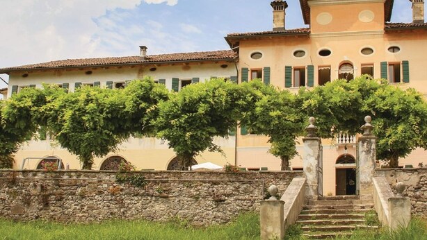 Un edificio grande e histórico con una escalera central, pared de piedra y abundante vegetación.