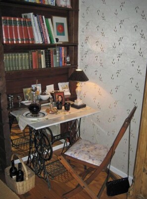 A small, cozy room with a wooden bookshelf filled with books, a sewing machine, a lamp, and a chair. - Anne's Holiday Home by the Lake (Belau)
