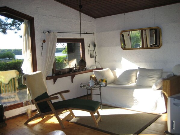 Una habitación acogedora con una mecedora de madera, un sofá, una mesita con un florero y una ventana con vistas a zonas verdes.