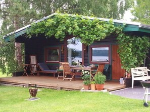 Una cabaña acogedora con un porche cubierto, muebles de madera y plantas en macetas.
