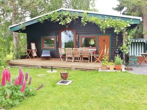 A wooden cabin with a deck, outdoor seating, and a garden with flowers. - Anne's Holiday Home by the Lake (Belau)