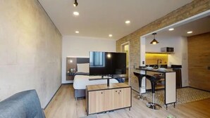 Un salon moderne doté d’un téléviseur à écran plat, d’un canapé, d’un meuble en bois et d’un coin repas avec une table et des chaises.