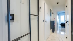 Een moderne hal met een digitale thermostaat, een deur met kaartslot en een uitzicht op een slaapkamer met een bed en balkon.