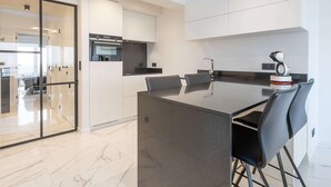 Een moderne keuken met een centraal eiland, zwarte stoelen en een robotstofzuiger.