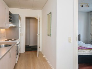 Cocina compacta con estufa, lavamanos y armarios, que da paso a un dormitorio con cama y ventana.