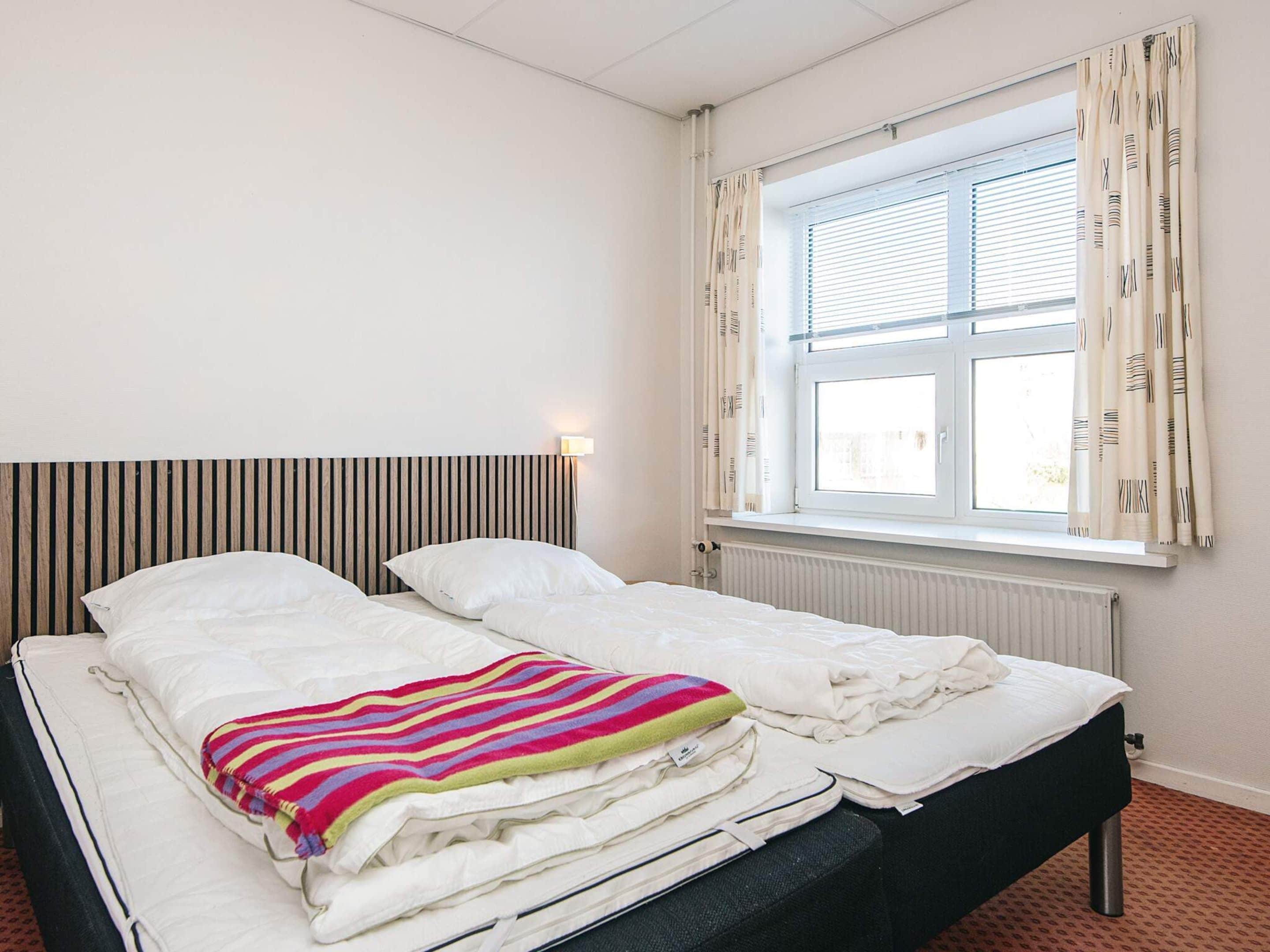 A double bed with a striped blanket, a bedside lamp, and a window with curtains.