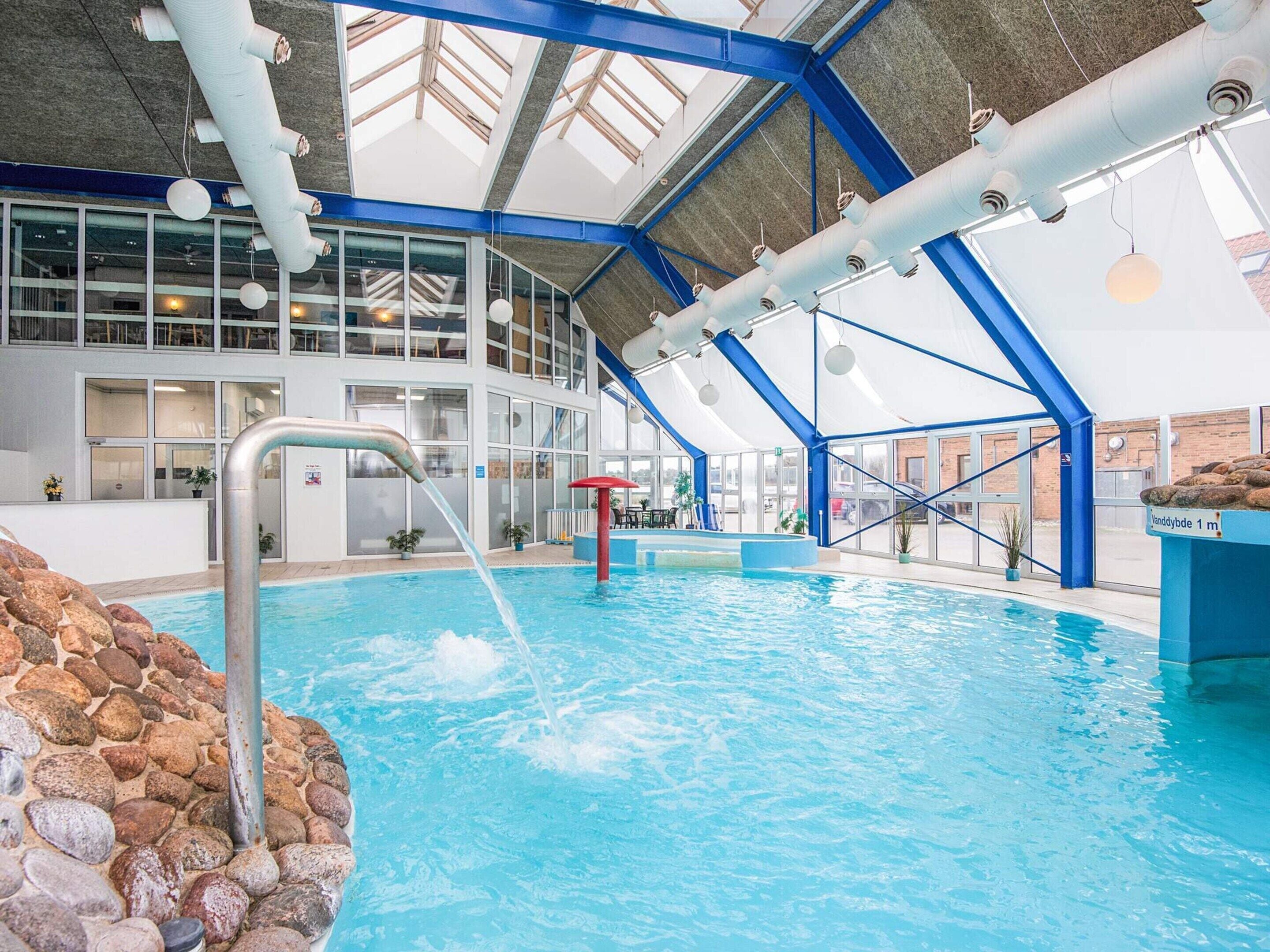 An indoor swimming pool with a clear view of the surrounding area, including a reception desk and a staircase leading to upper levels.