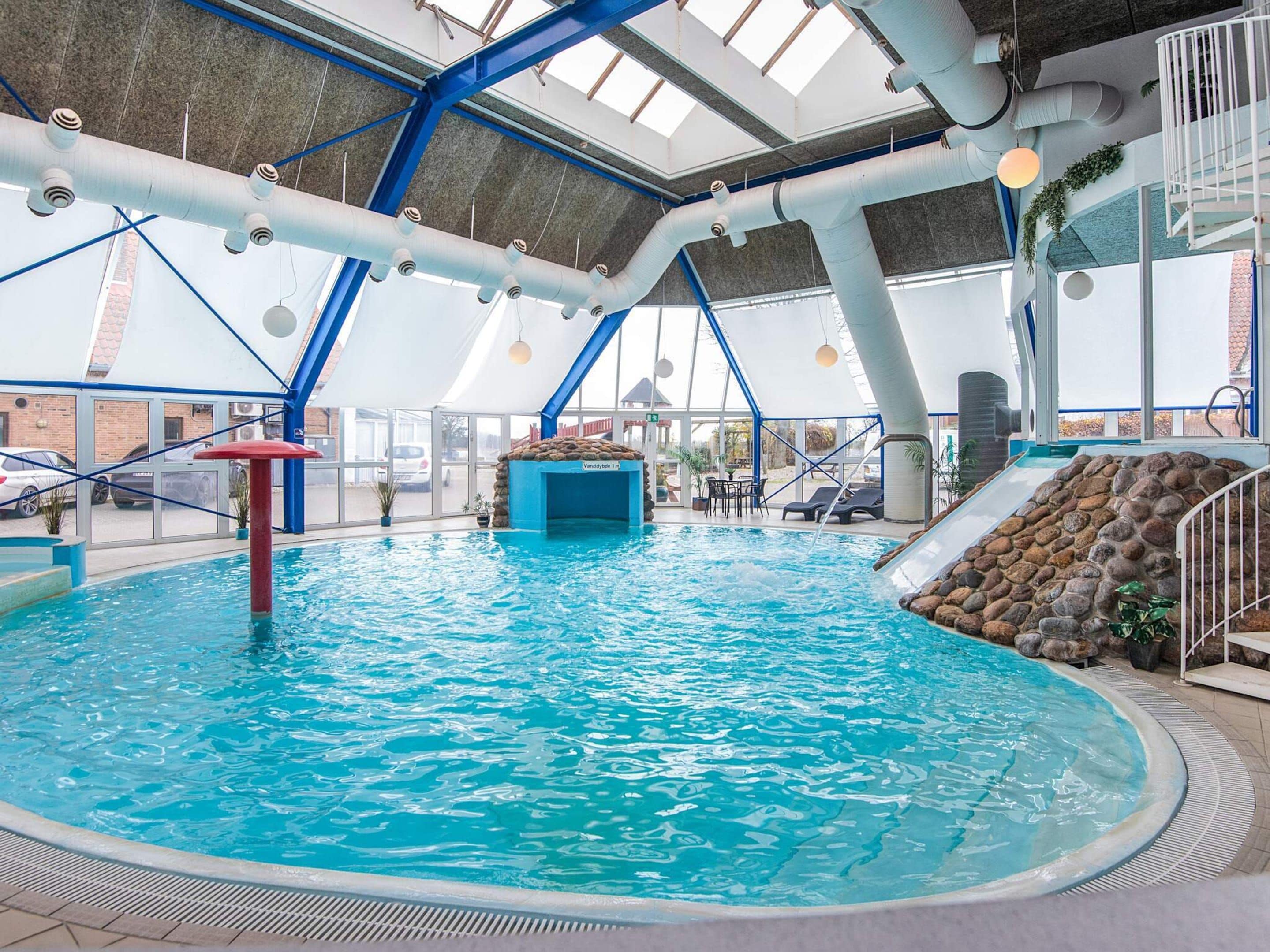 Ein Hallenbad mit Rutsche, Kletterwand und Sitzbereich mit Tischen und Stühlen.