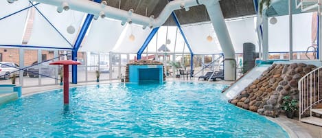 An indoor swimming pool with a slide, a rock wall, and a seating area with tables and chairs.