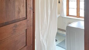 Una puerta de madera, una cortina blanca, una ventana y un lavamanos blanco.