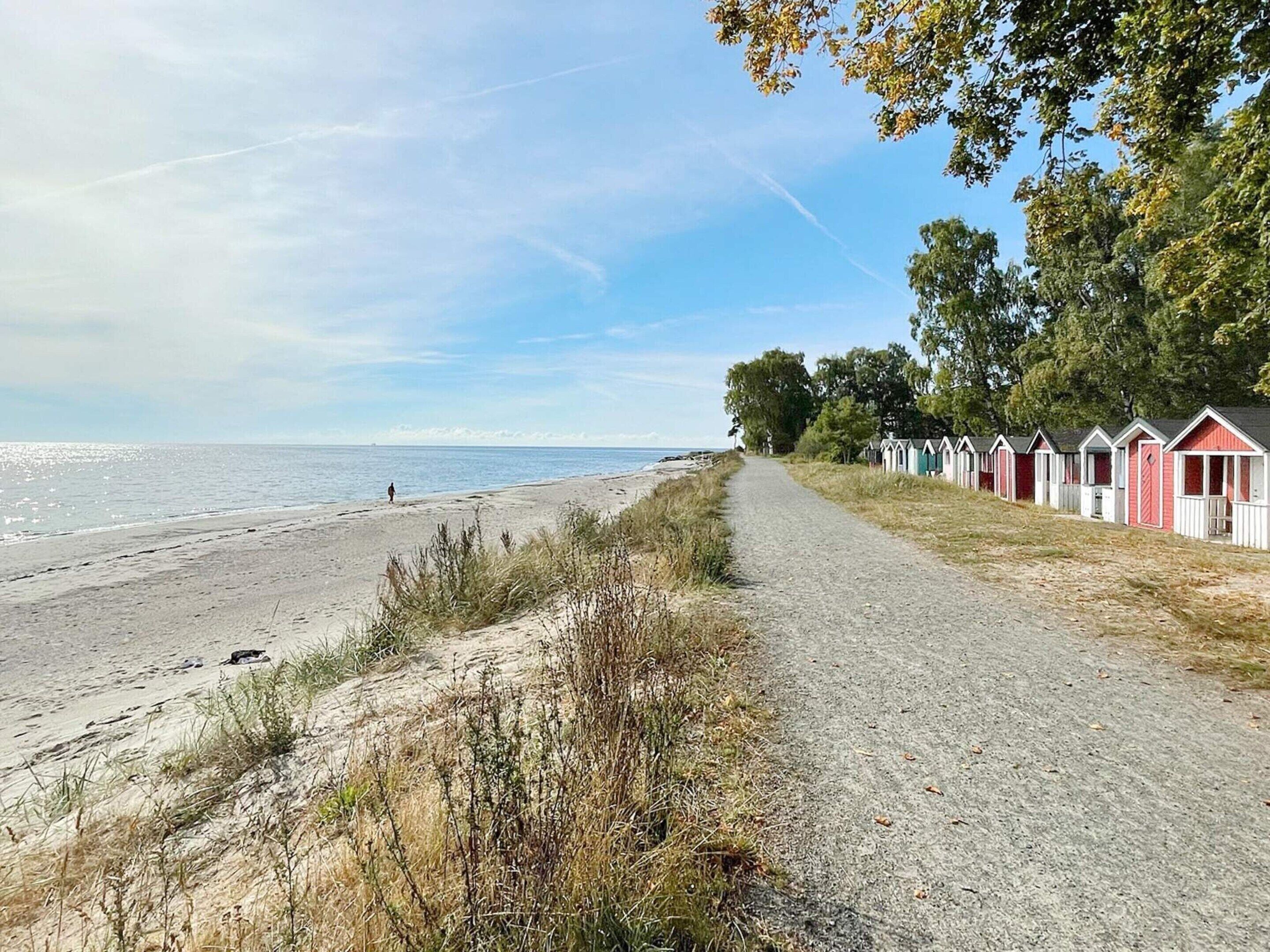 En sti langs stranden fører til strandhuse med kig ud over havet.