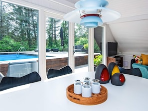 A modern living room with a pool view, a dining area with a wooden table, and a sofa with colorful cushions.