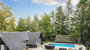 Ein modernes Haus mit geneigtem Dach, einem Schwimmbad und Gartenmöbeln.