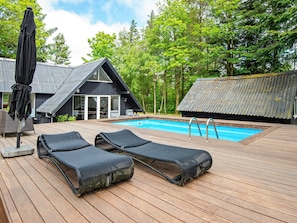 A wooden deck with two lounge chairs and a pool.