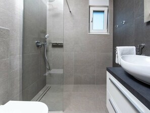Un baño moderno con cabina de ducha de vidrio, un lavabo blanco y una pequeña ventana sobre el espejo.