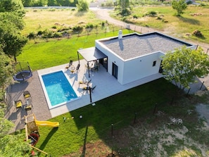 Una casa moderna con piscina, mobiliario de exterior y patio cercado.