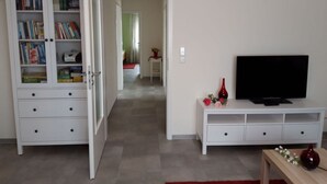 Ein Wohnzimmer mit einer weißen Unterhaltungseinheit, einem Fernseher und einem Bücherregal.