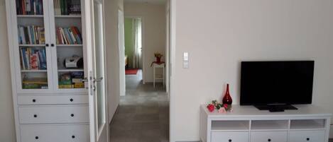 Una sala de estar con un mueble blanco para entretenimiento, un televisor y una estantería.