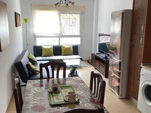 A modern living room with a sofa, dining table, TV, and washing machine. - Belvilla by OYO Bonita Casa en Aguadulce (Roquetas de Mar)