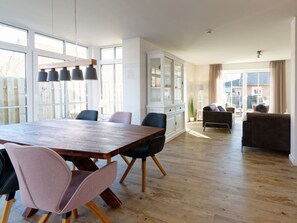A spacious living room with a large wooden dining table, several chairs, a sofa, and a cabinet. - Beach House Langeoog (Langeoog)