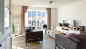 A modern living room with a sofa, a coffee table, a TV, and a speaker. - Beach House Langeoog (Langeoog)