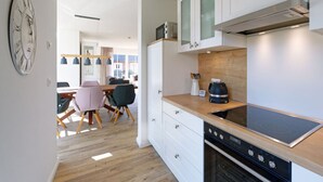 A modern kitchen with white cabinets, a built-in oven, and a wooden countertop. - Beach House Langeoog (Langeoog)