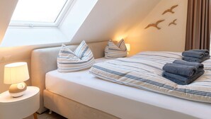 A bedroom with a skylight, a bed with striped bedding, pillows, a bedside lamp, and a wall with bird decorations. - Beach House Langeoog (Langeoog)