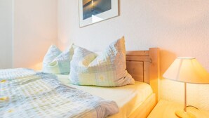 A neatly made bed with a patterned bedspread and pillows, a bedside table with a lamp, and a framed picture on the wall. - Sea View 4 - Villa Bella Vista (Sassnitz)