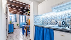 A kitchen with a patterned backsplash, a sink, and a stove. There is a blue curtain over the sink, and a plant is visible on the counter.