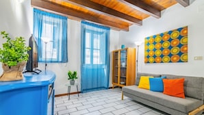 A living room with a sofa, blue curtains, a wooden ceiling, a TV, a cabinet, and a painting.